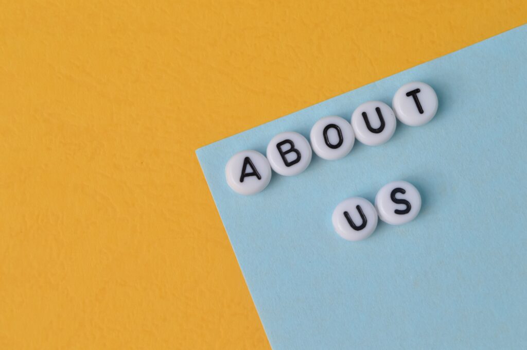 Flat lay of white letter beads spelling 'About Us' on blue and yellow background – representing dental practice storytelling and team introduction
