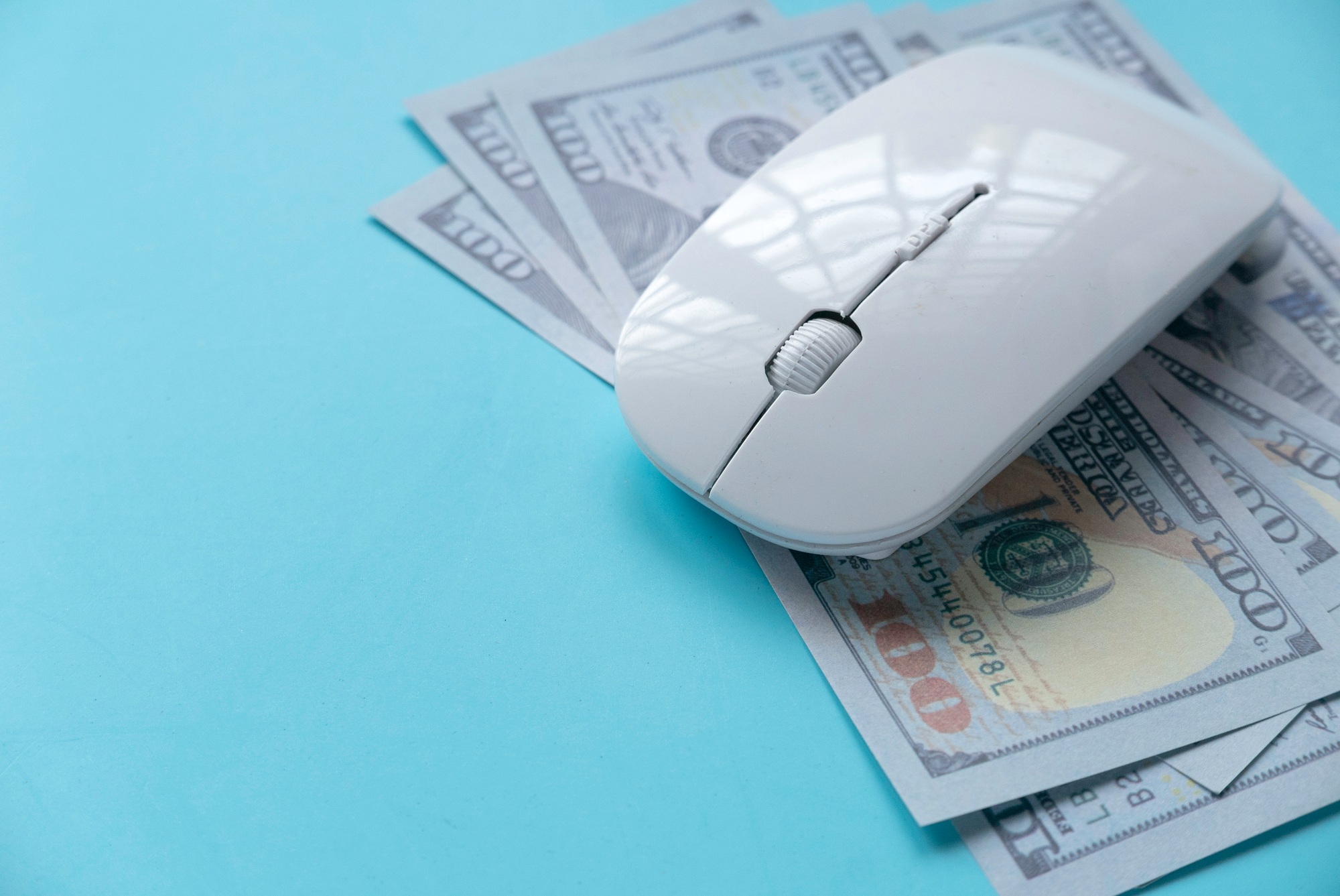 Computer mouse on top of hundred-dollar bills symbolizing pay-per-click (PPC) advertising costs for dental marketing campaigns